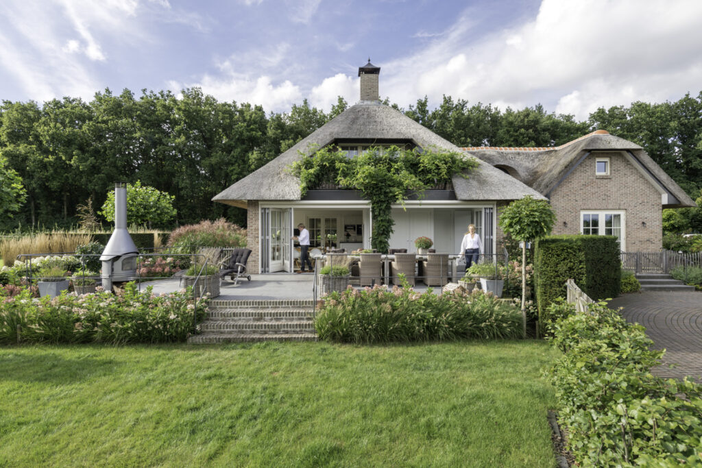 Blick aus dem Garten auf das hübsche, reetgedeckte Haus mit geöffneten Glas-Faltwänden