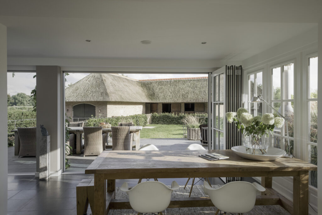 Blick aus dem Esszimmer durch die weit geöffneten Glas-Faltwände in den Garten hinaus. Die Glas-Faltwände wurden platzsparend an der Seite geparkt und geben die Aussicht frei.